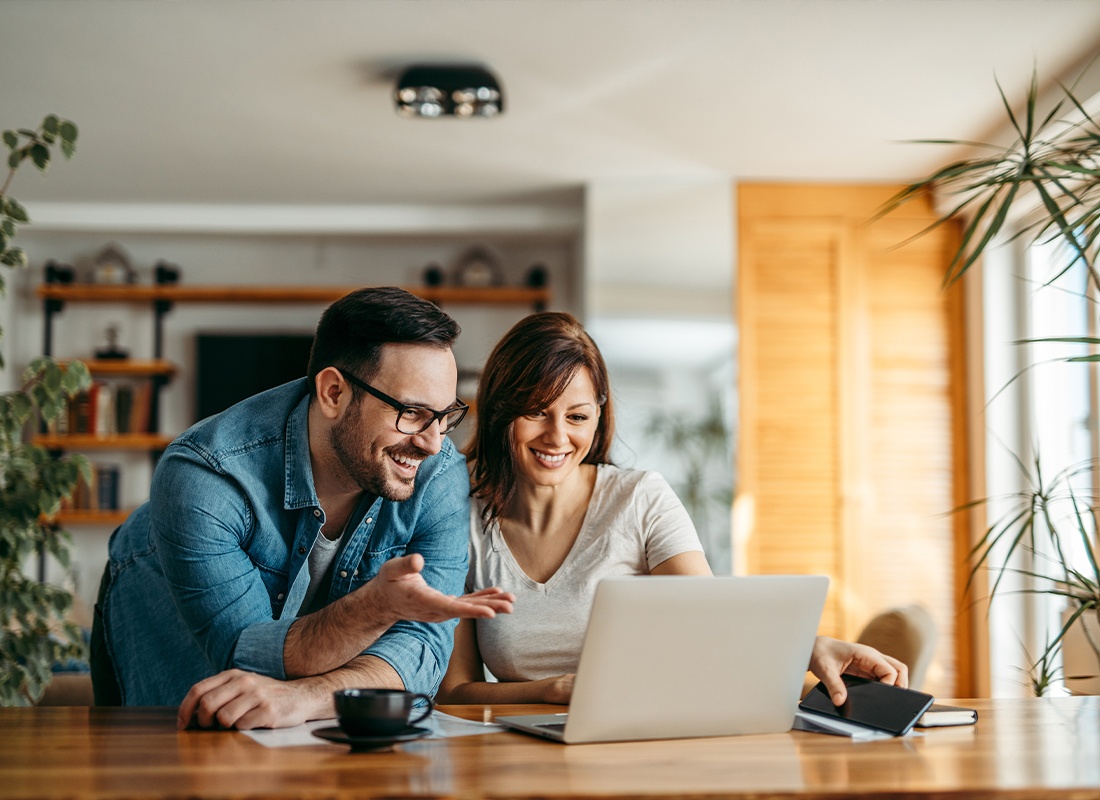 About Our Agency - A Young Couple Smiling While Looking at a Laptop at Home